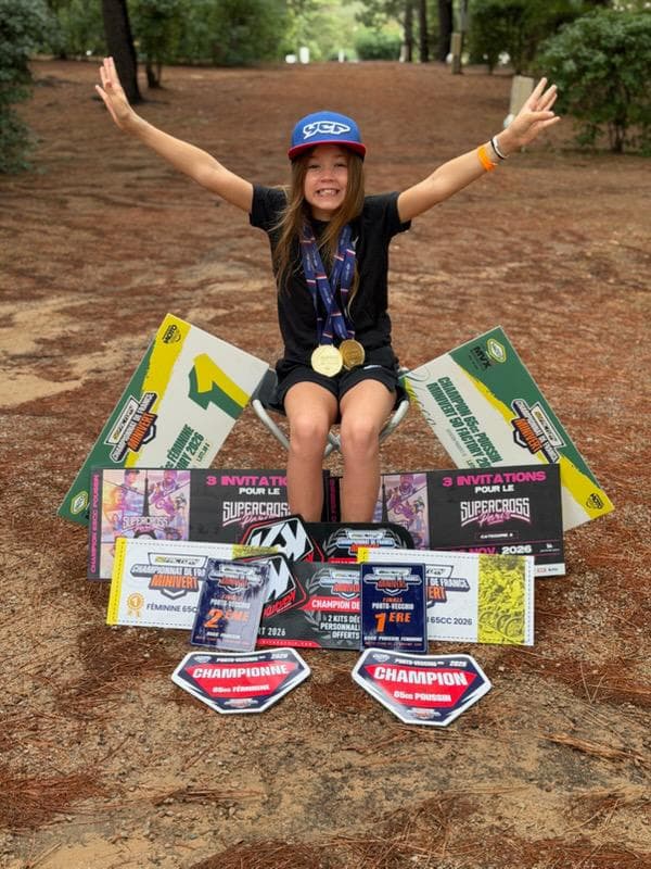 Emy Ochalek pose les bras levés derrière ses plaques et trophées de championne de France Minivert 2026