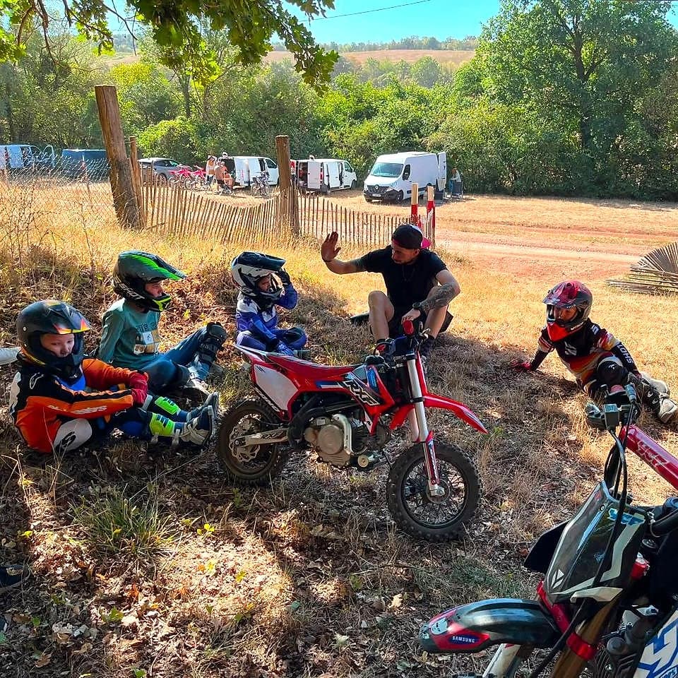 Le moniteur fait un point avec les jeunes pilotes à l'ombre, motos YCF du club au premier plan